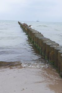 Wooden posts on beach against sky