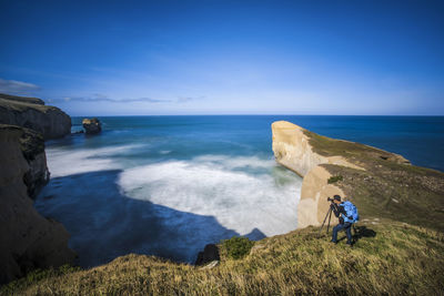Rear view of man on cliff by sea against sky