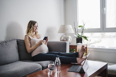 Midsection of woman using mobile phone while sitting on sofa at home