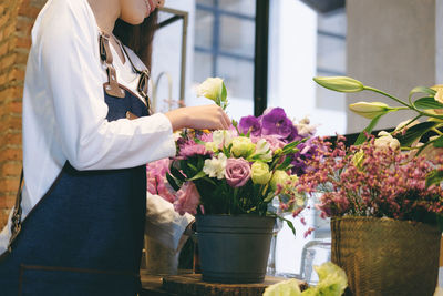 Midsection of woman touching flowers at shop
