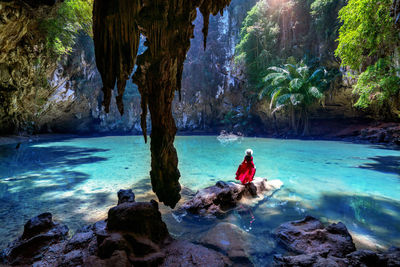 Rear view of woman sitting on rock by lake