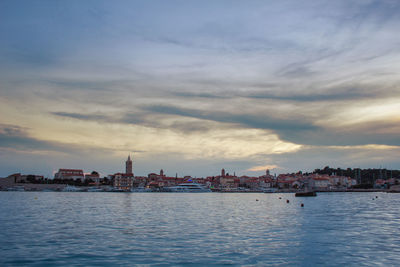 Buildings at waterfront against cloudy sky