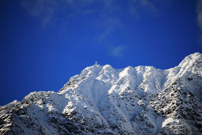 Low angle view of snowcapped mountains against blue sky