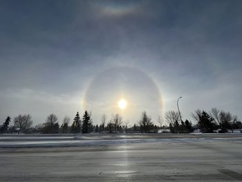 Scenic view of snow covered field against sky, with a majestic rainbow surrounding the sun
