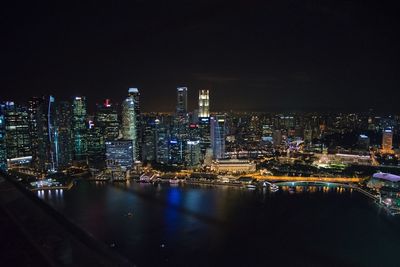 Illuminated buildings by river against sky at night