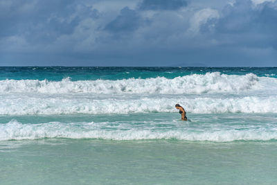 Woman standing in sea with waves on tropical beach with turquoise ocean