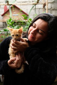 Young woman looks happily at her pet, a small yellow cat smiling.