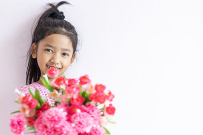 Portrait of smiling girl with pink flower against white background