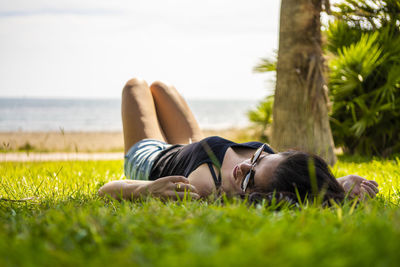 Surface level of young woman lying on grassy field against sea