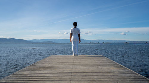 Rear view of man standing on pier over sea against sky