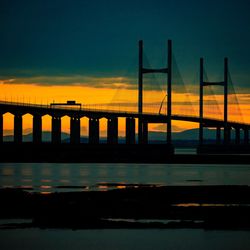 Silhouette bridge over river against sky during sunset