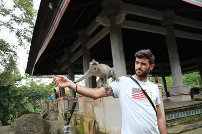 Young man holding horse standing against built structure