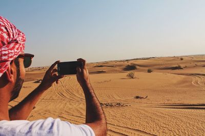 Man photographing on sand dune in desert against clear sky