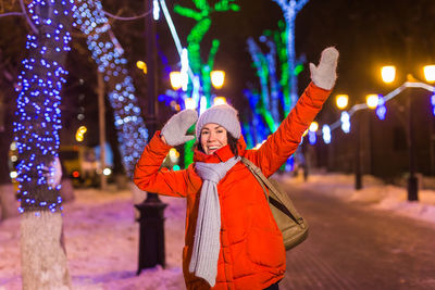 Portrait of woman standing against illuminated christmas tree