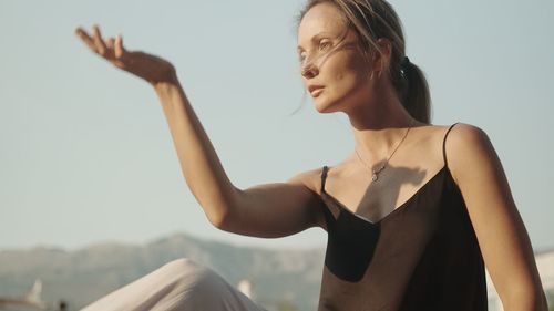 Portrait of young woman with arms raised against sky