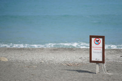 Close-up of information sign on beach against sky