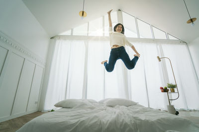 Full length of young woman jumping on bed at home
