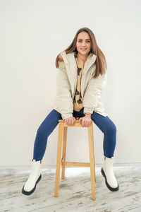 Portrait of a smiling young woman sitting against wall