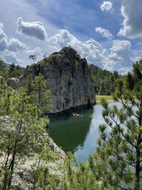 Kayak on calm lake with rock formation, clouds in sky, and pine trees