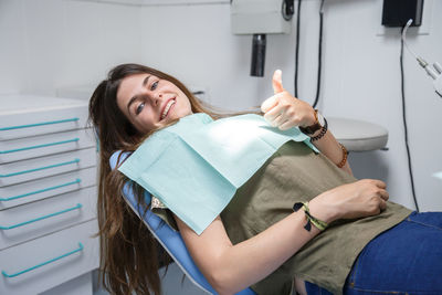 Portrait of smiling young woman showing thumbs up on dentist chair