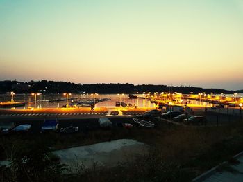 Cars on illuminated city against clear sky at sunset