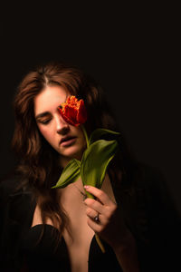 Close-up of woman holding flower against black background