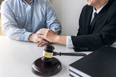 Close-up of lawyer and client with holding hands at desk in courtroom