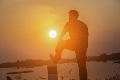 Silhouette man standing against orange sky during sunset