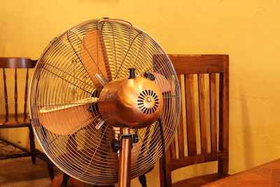 A vintage style fan in front of some wooden chair in a coffee shop