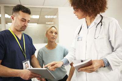 Nurse and doctor discussing over tablet pc by senior patient in medical room