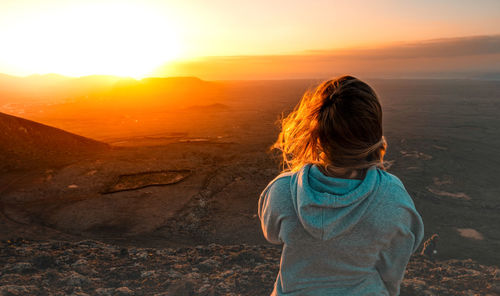 Rear view of woman standing on land against sky during sunset