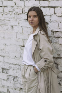 Portrait of young woman standing against brick wall