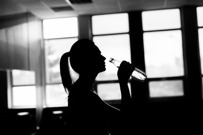 Side view of silhouette woman drinking glass window