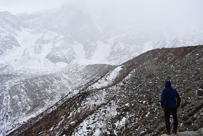 Rear view of person standing on snowcapped mountain