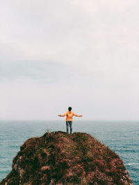 Rear view of man standing on cliff against sea