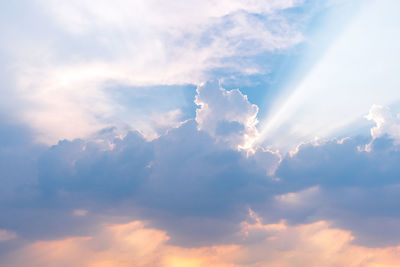 Low angle view of sunlight streaming through clouds