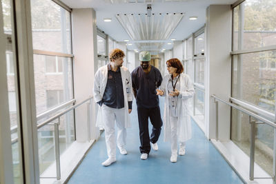 Full length of senior female doctor discussing with colleagues while walking in hospital corridor