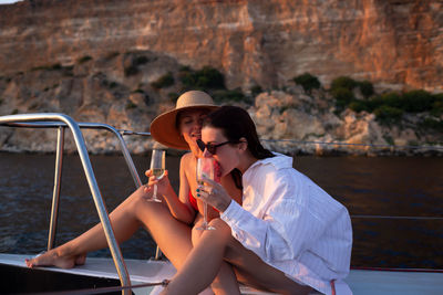 Cheerful women holing drink sitting on boat deck