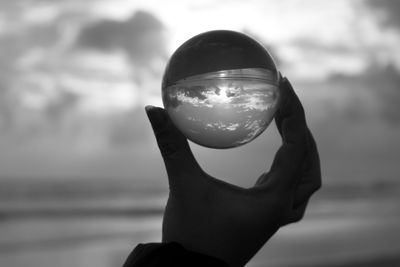 Close-up of hand holding crystal ball against sky