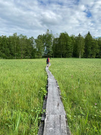 Woman walking on dirt road amidst field against sky