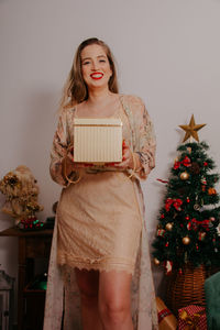 Portrait of smiling young woman holding christmas tree at home