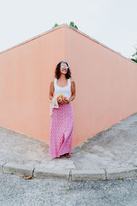 Woman standing by pink umbrella against wall