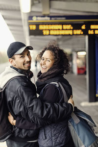 Side view portrait of happy couple with arms around on subway platform