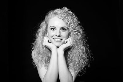 Portrait of smiling woman with curly hair against black background