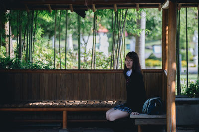 Portrait of young woman sitting on bench against window