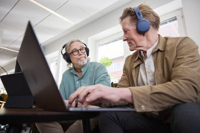 Senior men talking to each other while sitting in living room and using laptop to edit podcast