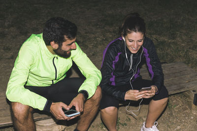 Sportswoman and male athlete using smart phone while sitting on bench in park