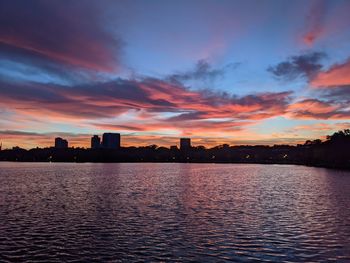 Silhouette buildings by lake against sky during sunset