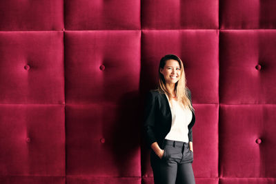 Portrait of smiling young woman standing against wall