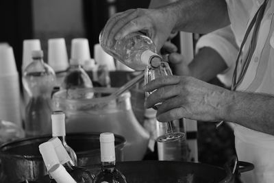 Midsection of bartender pouring drink from bottle into wineglass